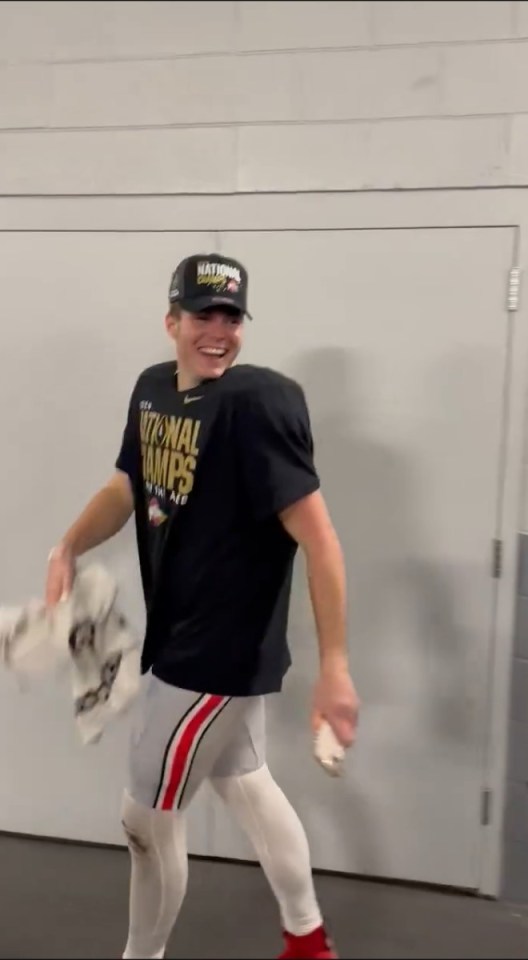 A smiling man in a National Champs shirt and hat walks down a hallway.